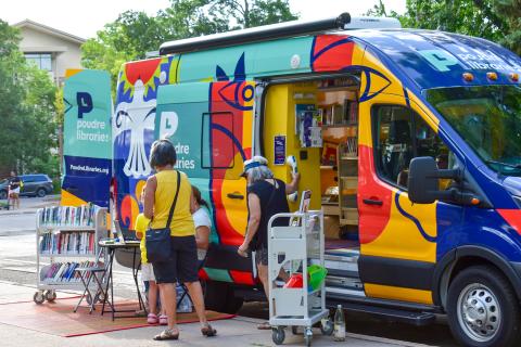 Evie, the Mobile Library, parked at an event with the doors open. Patrons browse the collection and talk with staff.