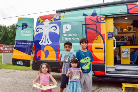 Four kids stand outside Evie, the Mobile Library, holding books they just picked out