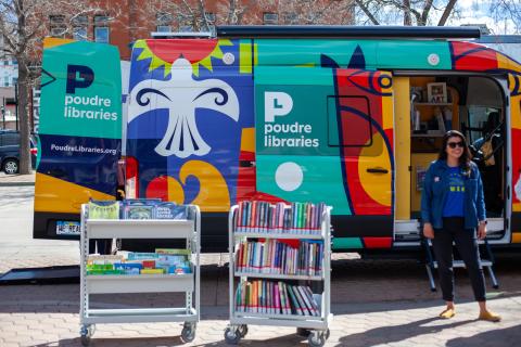 Evie, the Mobile Library, parked at an event with the doors open and book carts on the sidewalk