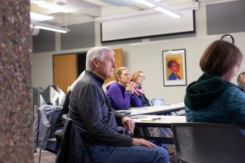 Four people face a not-shown presenter and listen to presentation