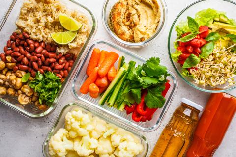 View from above of colorful ingredients including vegetables, grains and sauces placed into individual meal dishes. 