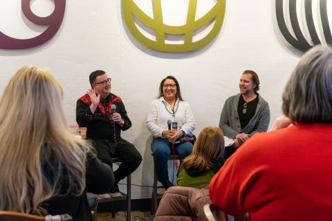 Three adults face the crowd and camera as part of an author panel