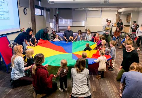 Kids and adults lift colorful parachute off the floor