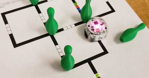 Ozobot moves around green game pieces on a track