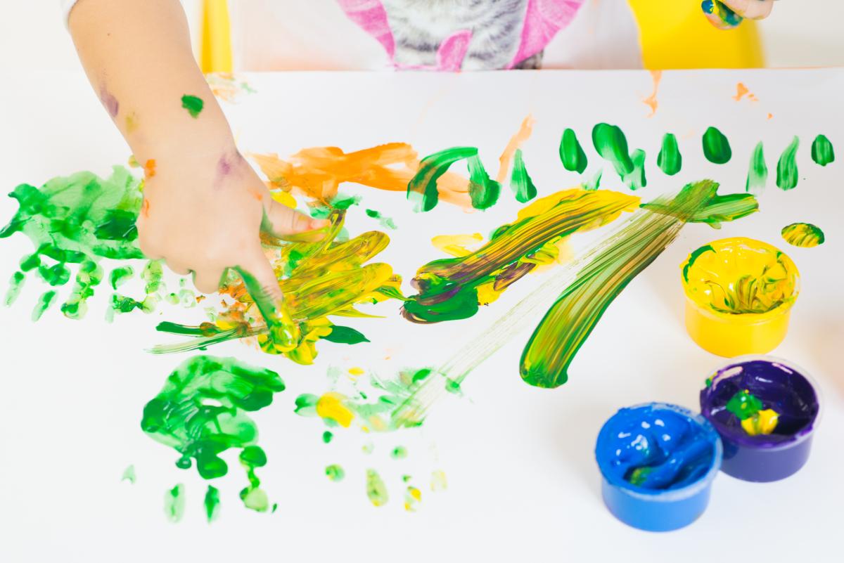 Child's hands playing with green, blue, and yellow paint